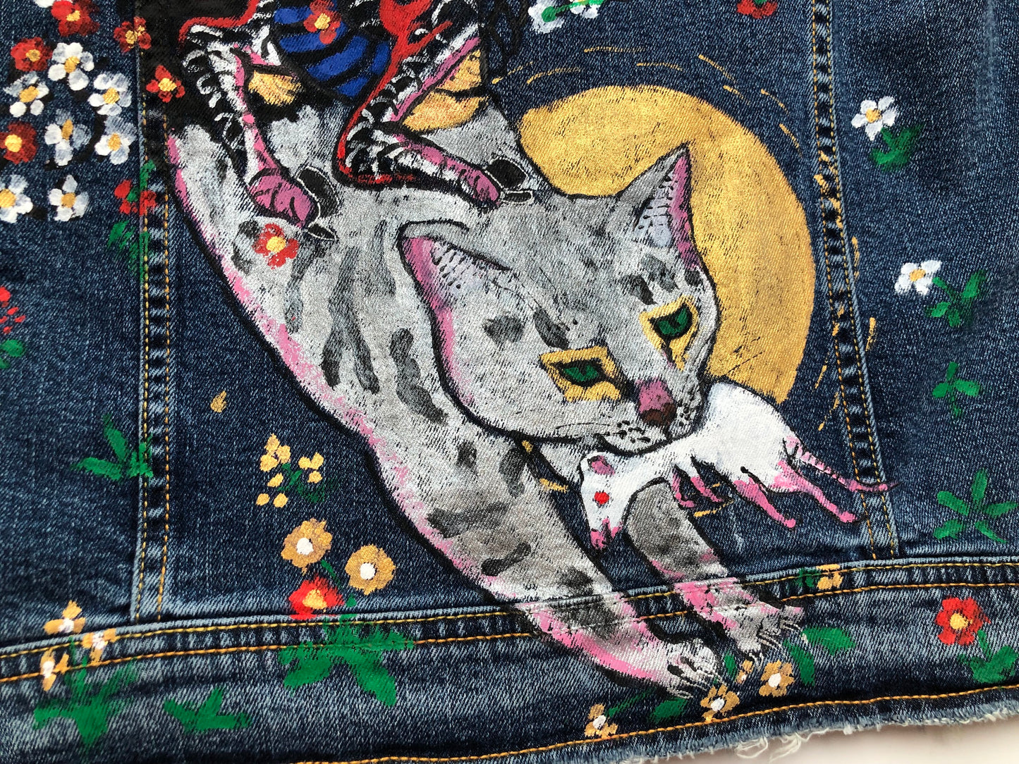 A jumping cat with a mouse in its teeth and a demon's hooves on a women's denim jacket