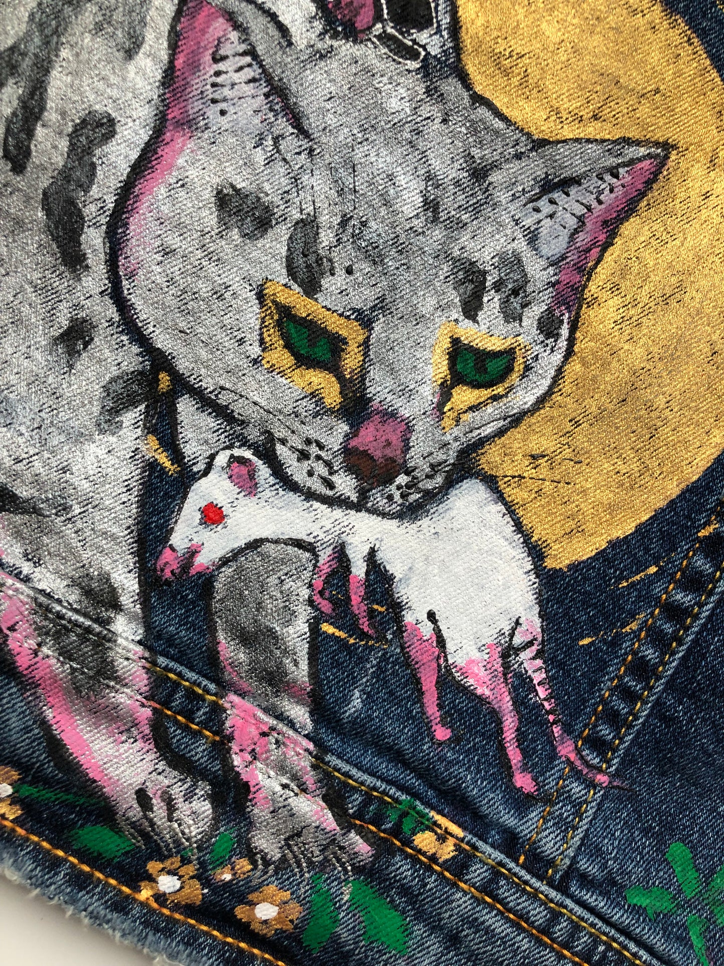 The muzzle of a cat in detail with a mustache, claws and a mouse on a women's denim jacket