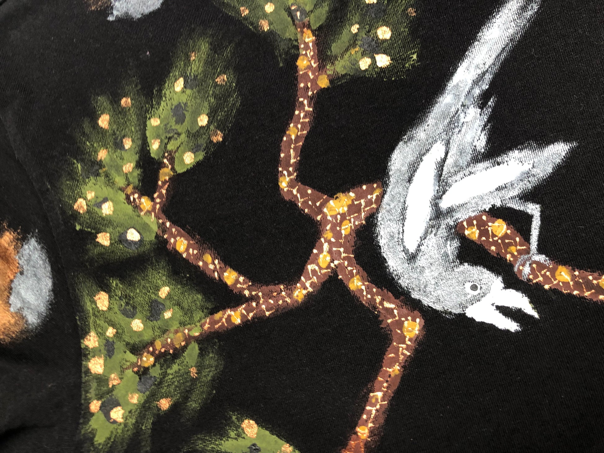 Detail of a tree branch with foliage and a bird. Brown branch with golden bark and black pearl bird on a t-shirt