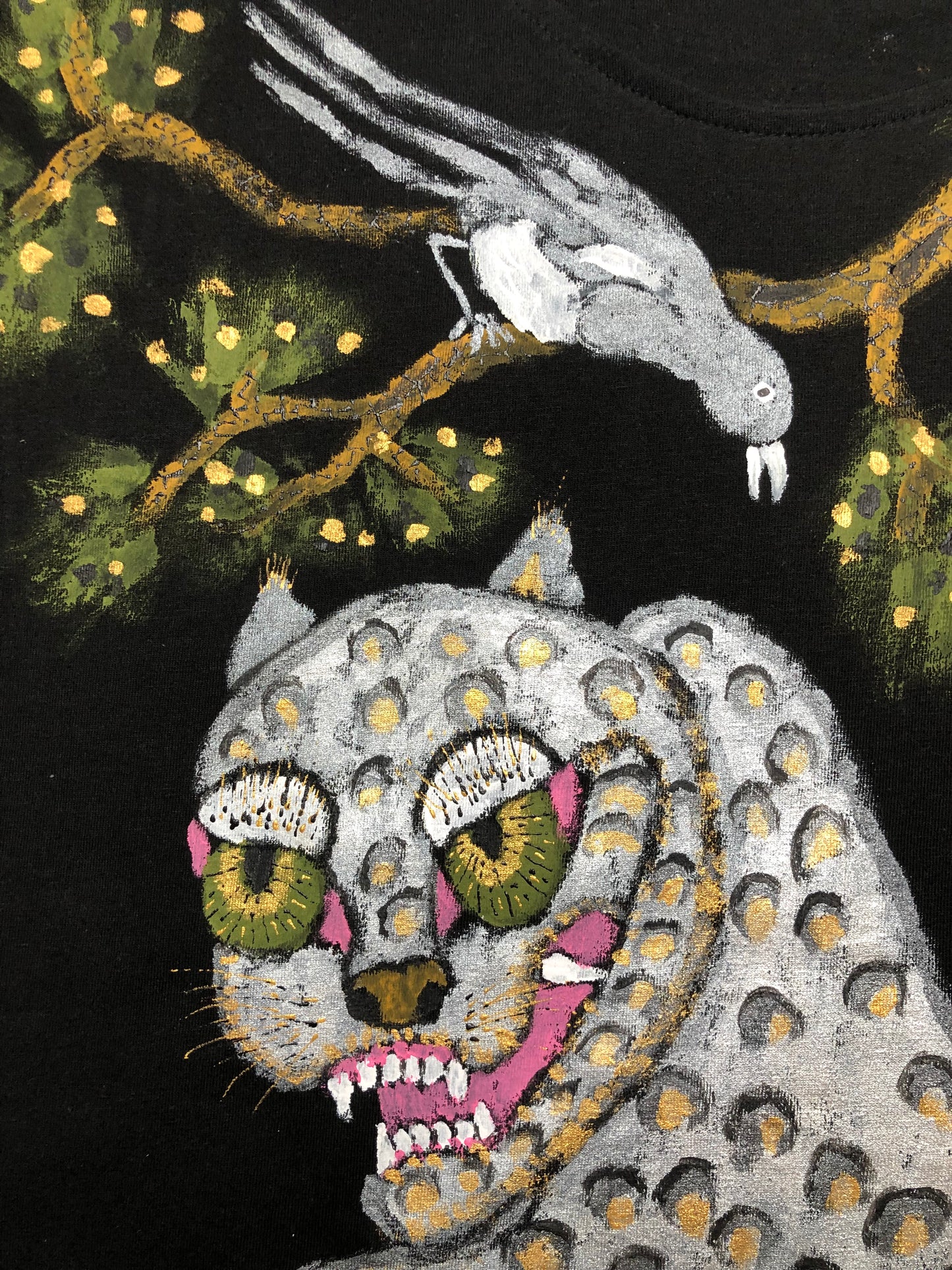 The muzzle of a silver leopard with a bird on a tree in detail on a women's black t-shirt